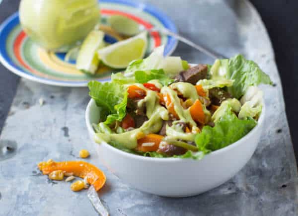 Overall, this steak fajita salad is the type of dish that is yummy for adults, you can easily change of the flavors to your own family's favorites, and it's easy for kids to build it themselves and get excited about the foods. And could I just mention that the avocado sauce is amazing? Steak fajita salad in a white bowl on a gray tray.