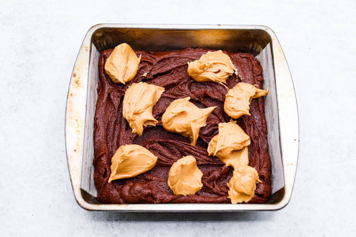 The best of both worlds collide in these peanut butter brownies! Fudgy homemade brownies are swirled with a sweet peanut butter mixture. The combination is an explosion of rich decadent flavors! Seventh photo of the peanut butter mixture dolloped on top of the brownie batter.