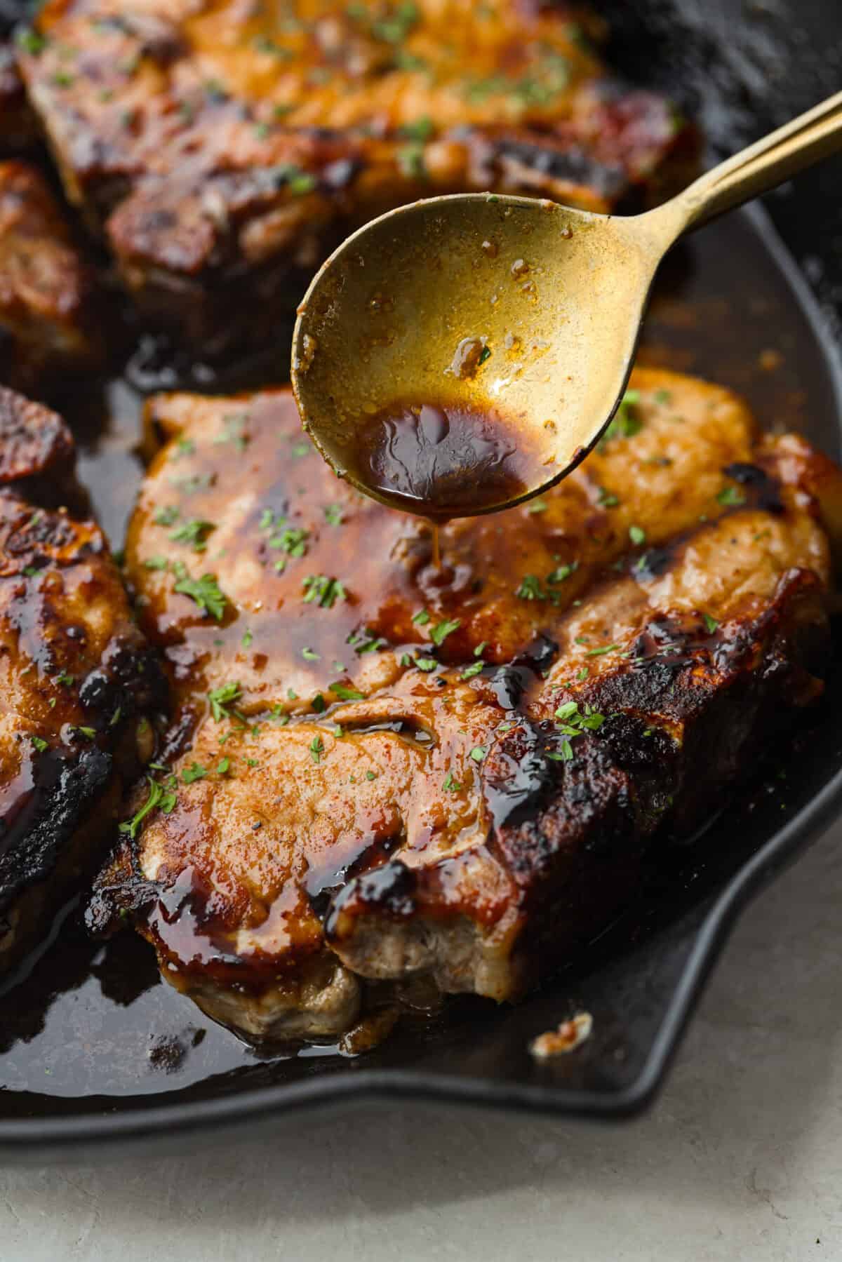 These brown sugar glazed pork chops are incredibly flavorful and delicious. Your family will love the salty pork smothered in a sweet brown sugar glaze. The crispy seared textured with the sweet sauce dripping down each bite will have you begging for more! Close up shot of someone pouring glaze over pork chop.