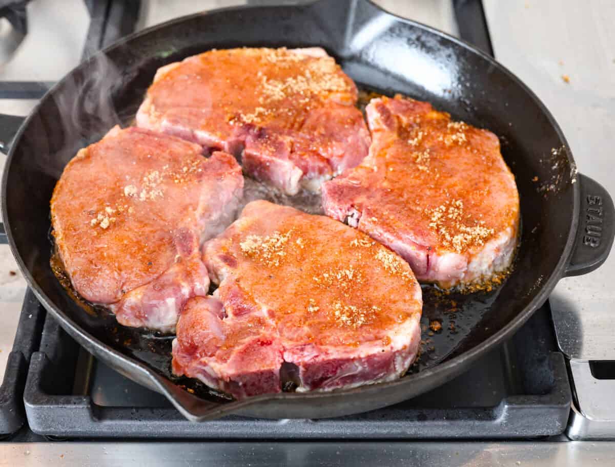 These brown sugar glazed pork chops are incredibly flavorful and delicious. Your family will love the salty pork smothered in a sweet brown sugar glaze. The crispy seared textured with the sweet sauce dripping down each bite will have you begging for more! Overhead shot of pork chops searing in a skillet on a stove top.
