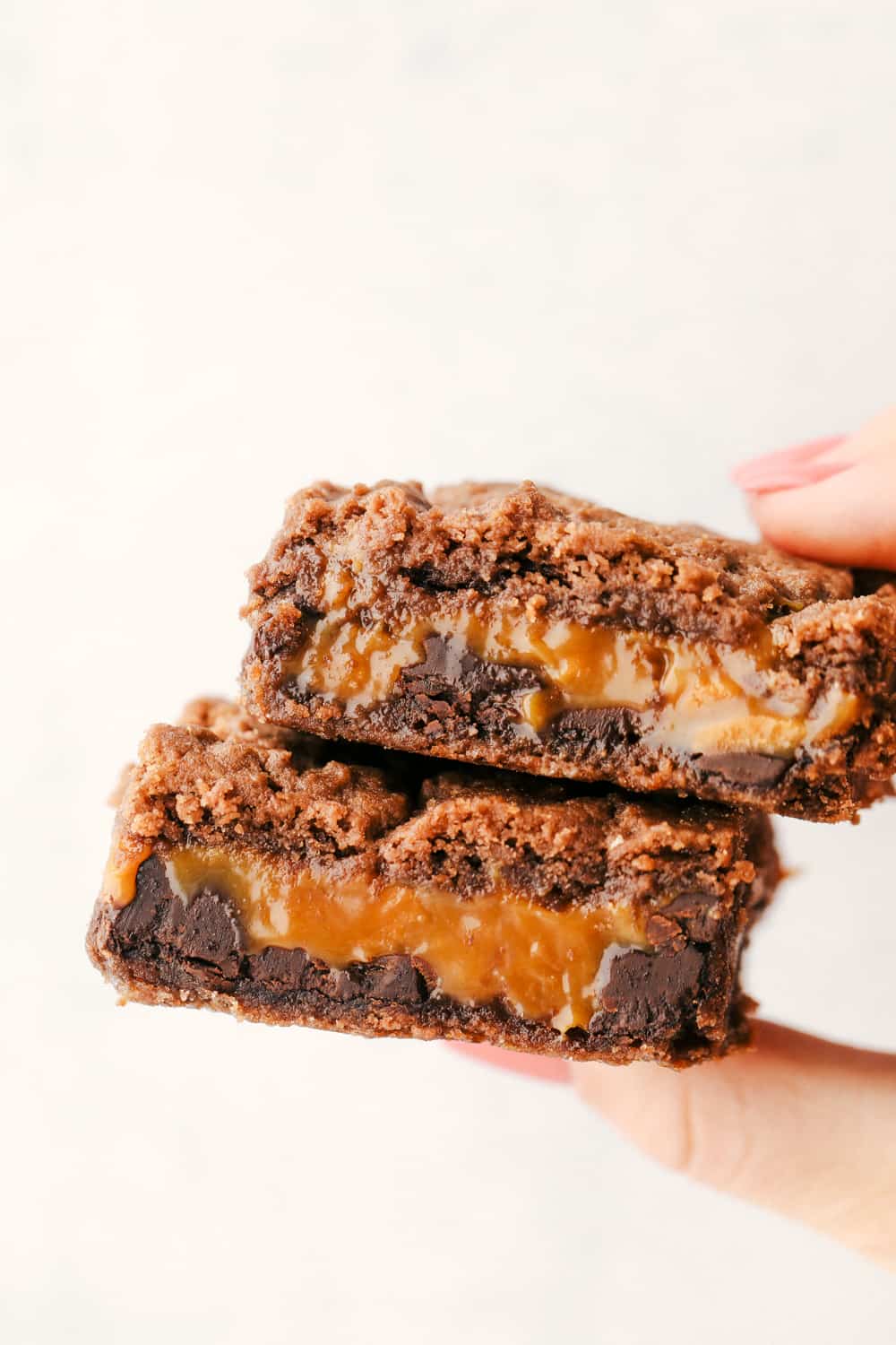 Caramel brownies just got easier! Made with cake mix and melted caramel candies, they’re rich, gooey, egg-free, and fuss-free. This will be your new favorite shortcut dessert! Holding two ooey gooey caramel brownies.