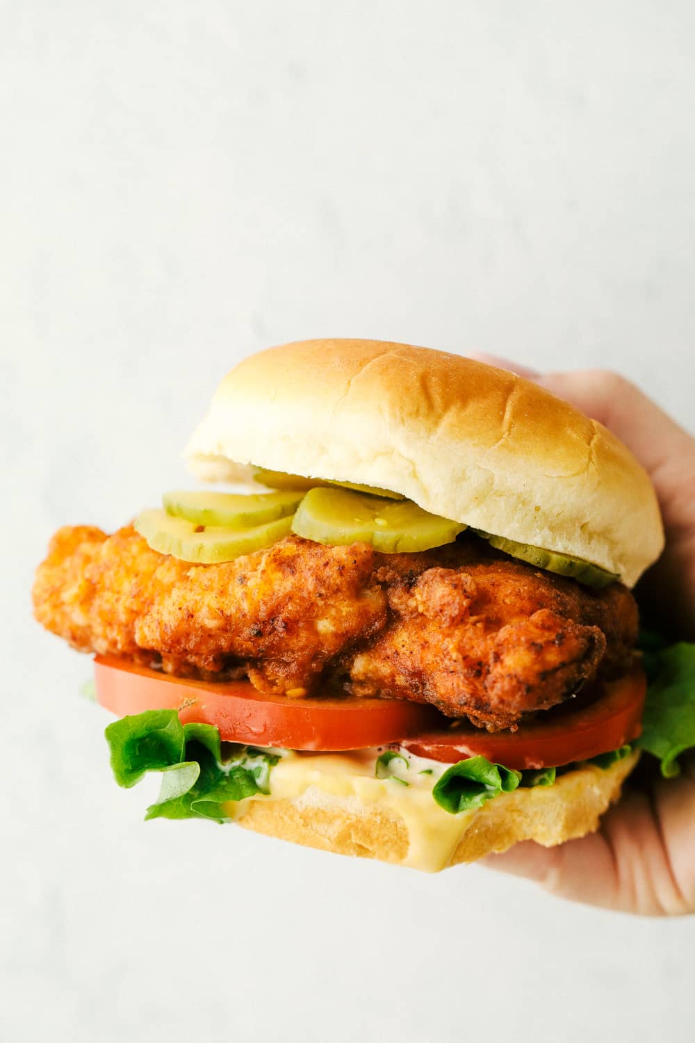 Chick-fil-A sandwiches are just as tender and juicy as the original, only better!ย Now you can satisfy your craving for those perfectly breaded and seasoned sandwiches anytime you need to! Holding a chicken sandwich with pickles, lettuce and tomatoes.