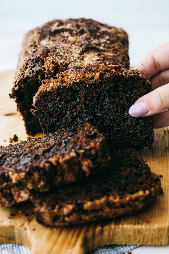 Chocolate Zucchini Bread is moist, sweet and filled with a hidden gem! It bakes perfectly and has a beautiful cracked sugar crust topping! Chocolate zucchini bread sliced in three pieces on a cutting block.