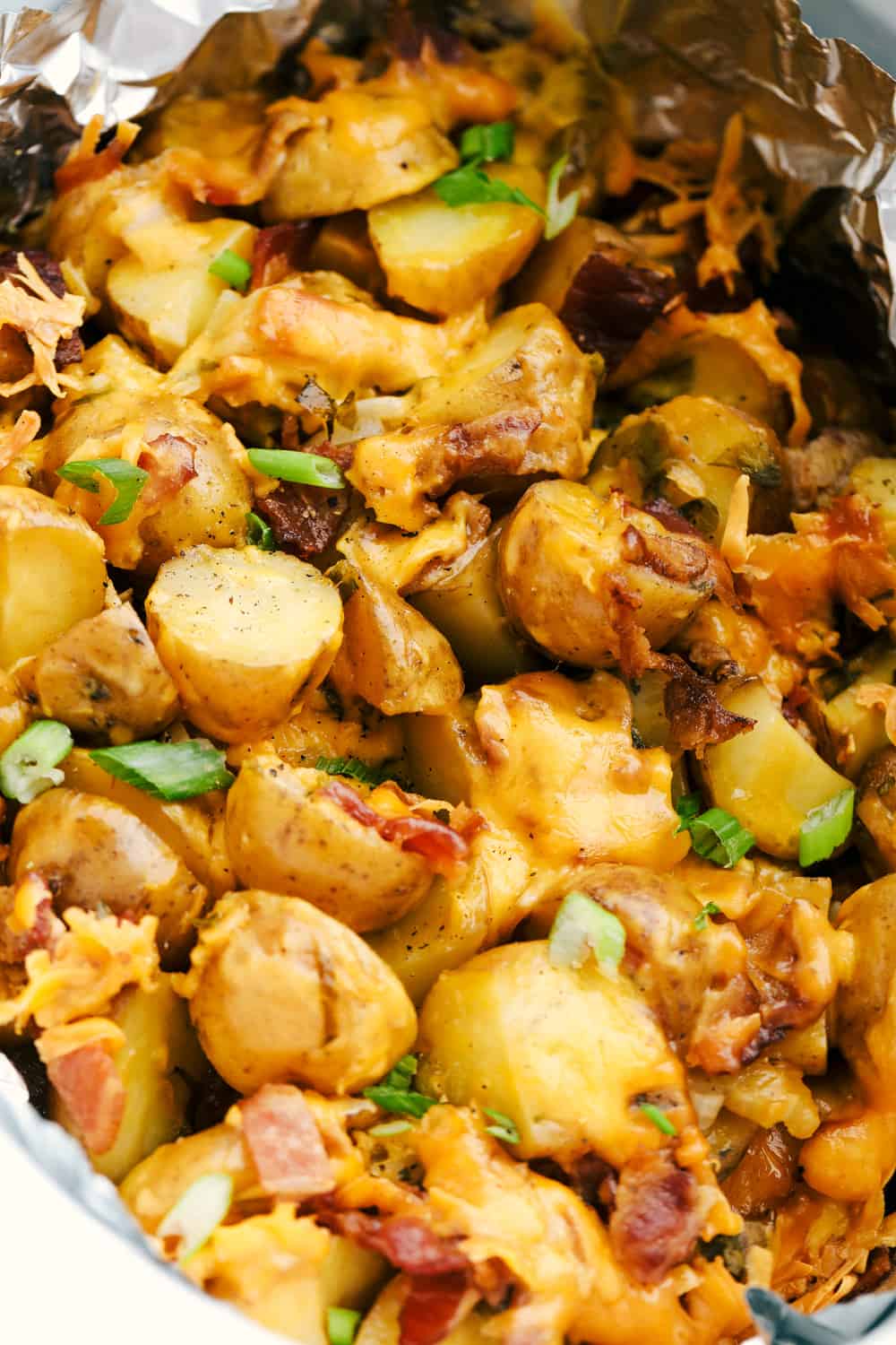 Perfectly tender and packed with flavor. All of the flavors combined with cheese and bacon to create these perfectly tender and delicious potatoes. Up close photo of the cheesy ranch bacon potatoes in a slow cooker with foil.