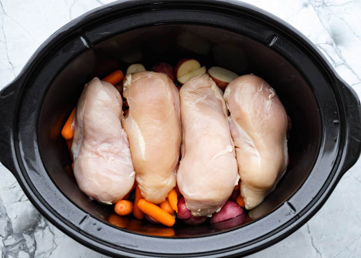 My Slow Cooker Creamy Ranch Chicken takes 10 minutes of prep and uses 6 simple ingredients. It's so good your whole family is going to love it, even your picky eaters! Overhead shot of vegetables and chicken breasts in the bottom of the crockpot.