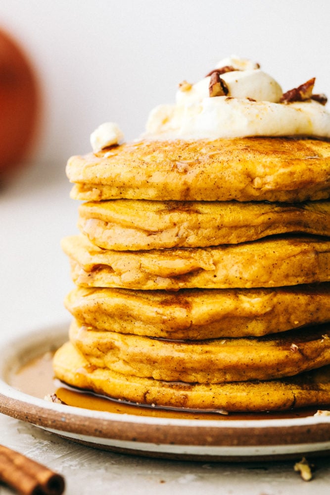 Fluffy and moist pumpkin spice pancakes are what fall breakfast dreams are made of! Perfectly spiced and full of flavor, it's like having pumpkin pie for breakfast! Close side view of a stack of pumpkin spice pancakes. Whipped cream and pecans are garnished on the top pancake.