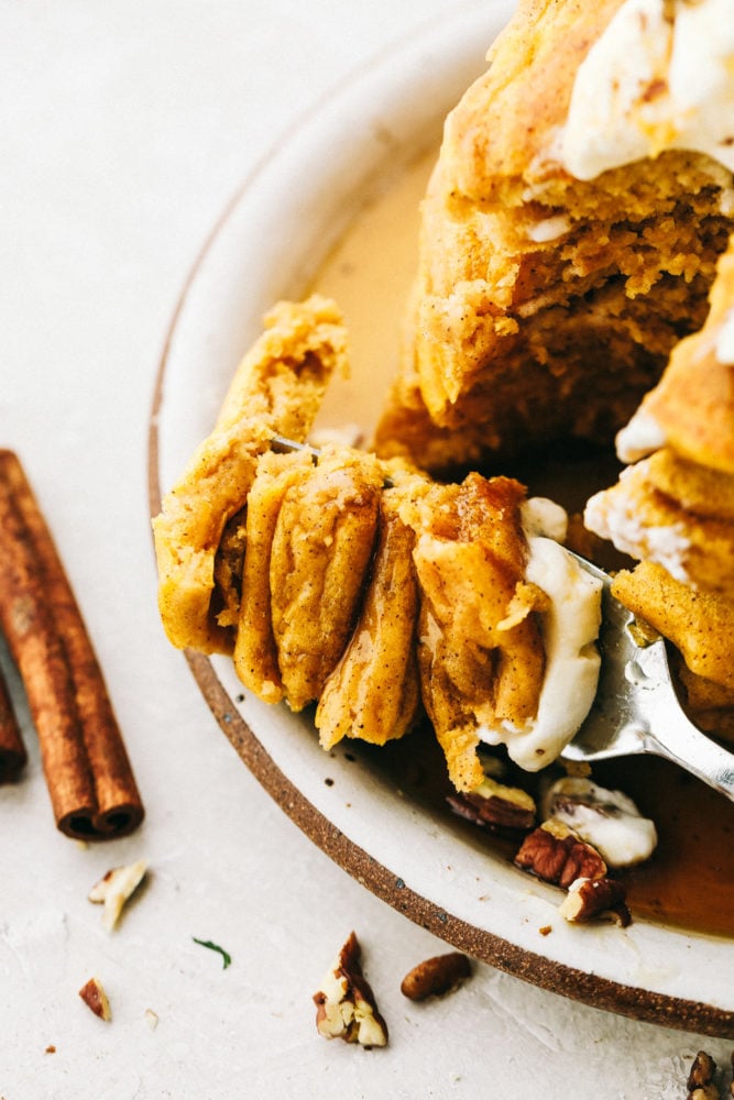 Fluffy and moist pumpkin spice pancakes are what fall breakfast dreams are made of! Perfectly spiced and full of flavor, it's like having pumpkin pie for breakfast! Top close view of a fork cutting into a stack of pumpkin spice pancakes.