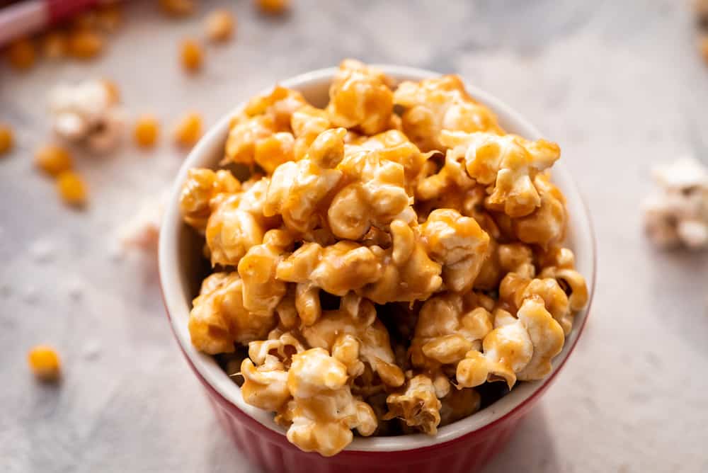 Amazing Salted Caramel Popcorn is a sweet and salty snack with melted caramel covering each popcorn for a soft, crunchy, rich and chewy snack! The Ultimate Sweet and Savory Snack! salted caramel popcorn in a red bowl