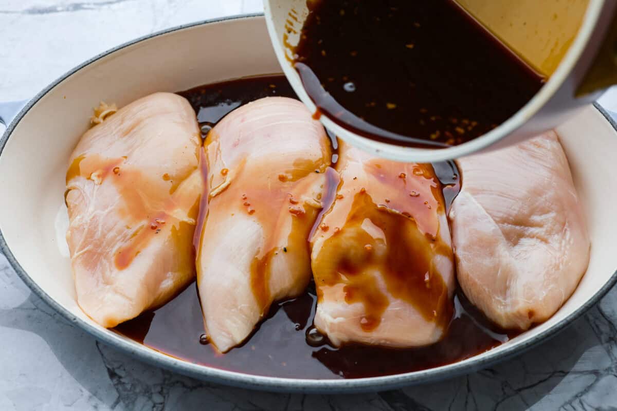 Baked teriyaki chicken is a healthy, delicious dish that comes together in just 45 minutes! The tender, moist chicken is drenched in a sweet and savory teriyaki glaze. Perfect served over some rice and a side of veggies, and the best partโฆ the entire family will love it! Overhead shot of sauce being poured over chicken breast.