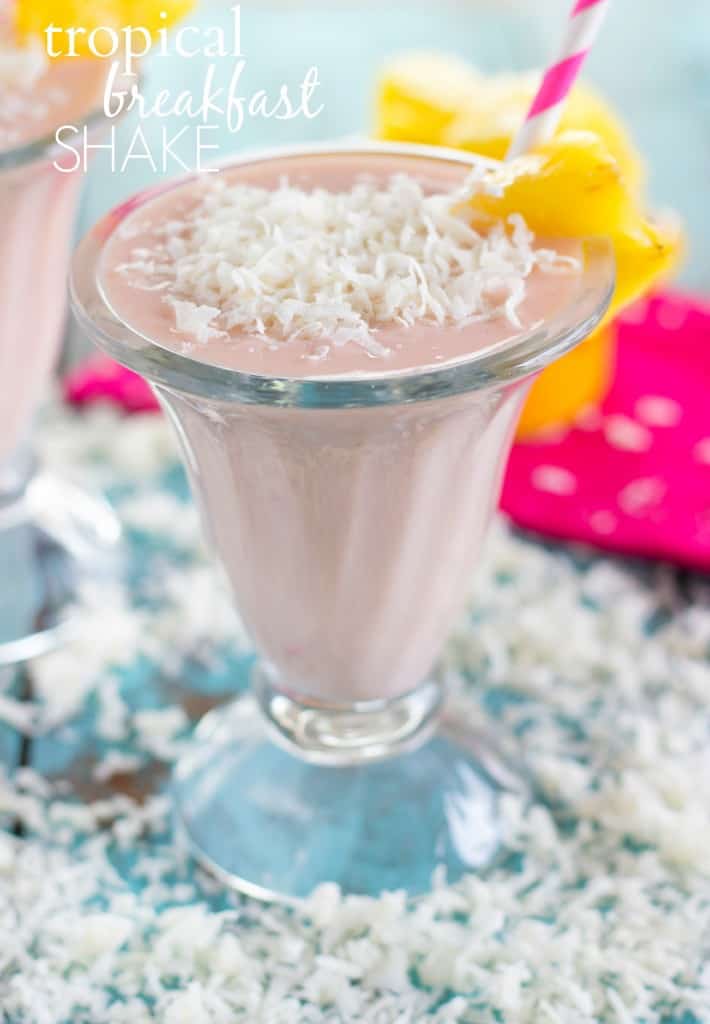 This shake has all kinds of tropical flavors โ fresh pineapple, orange juice, a ripe banana, and some coconut flakes to top it all off. It tastes like summer in a glass! Tropical Breakfast Shake in a glass cup with a pink straw and coconut shaving on the side.