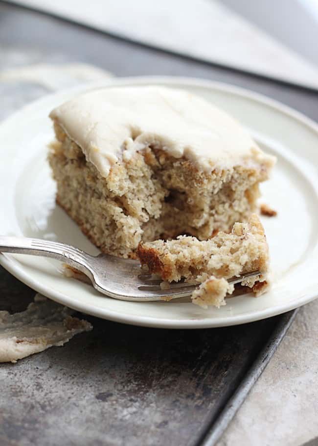 Moist browned butter banana cake with a sweet and simple brown sugar frosting! The perfect way to use up those browning bananas on your counter! Browned Butter Banana Cake with Brown Sugar Frosting on a white plate with a fork taking a bite out of it.