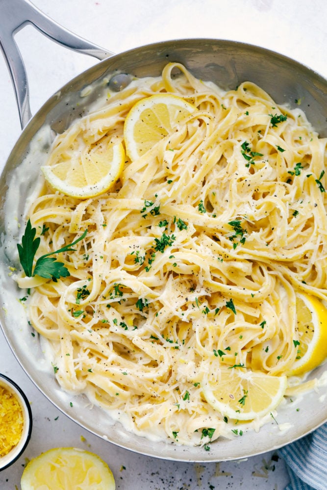 Lemon Garlic Cream Fettuccini is a quick meal that is loaded with rich flavors that taste like they took all day to create, but are ready in under 30 minutes. This will be a huge hit recipe that your entire family will go crazy over! Lemon Garlic Cream Fettuccini in a frying pan with sliced lemon mixed in.