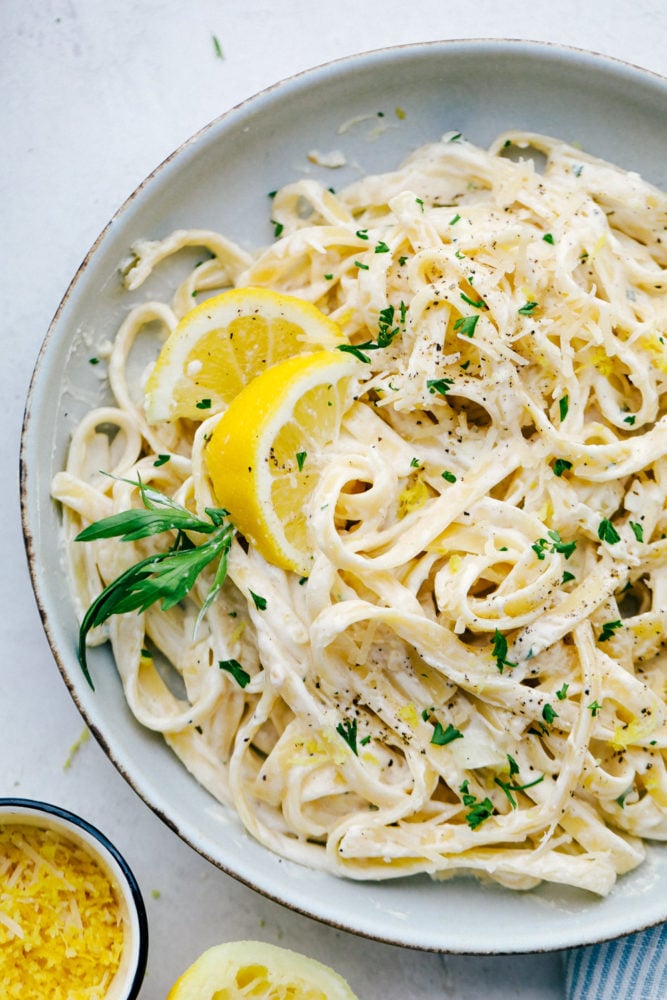 Lemon Garlic Cream Fettuccini is a quick meal that is loaded with rich flavors that taste like they took all day to create, but are ready in under 30 minutes. This will be a huge hit recipe that your entire family will go crazy over! Lemon Garlic Cream Fettuccini on a white plate.