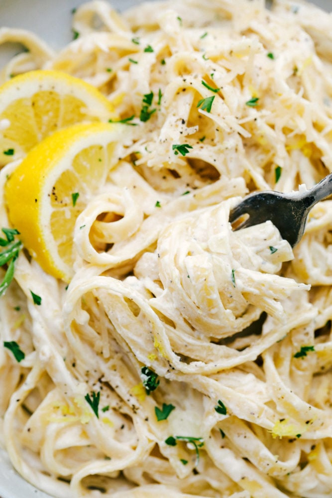 Lemon Garlic Cream Fettuccini is a quick meal that is loaded with rich flavors that taste like they took all day to create, but are ready in under 30 minutes. This will be a huge hit recipe that your entire family will go crazy over! Close up of Lemon Garlic Cream Fettuccini with a fork removing some.