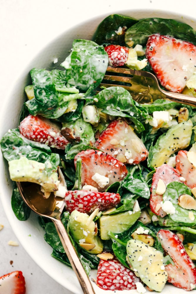 Fresh strawberries, sliced avocados, slivered almonds and sprinkled with feta cheese all tossed with a spinach salad then drizzled poppyseed dressing mixed together for the final touch. This strawberry avocado spinach salad is one everyone is raving about! Strawberry avocado spinach salad with poppyseed dressing tossed together and put in a bowl with a fork and spoon.