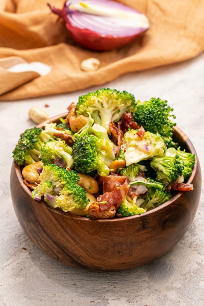 Broccoli Cashew Salad is a perfect cool and crunchy salad filled with savory bacon crumbles, cashews and broccoli, all covered in an amazing dressing. You will be making this all the time once you see how easy and delicious it is! Cashew Broccoli Salad in a wooden bowl.
