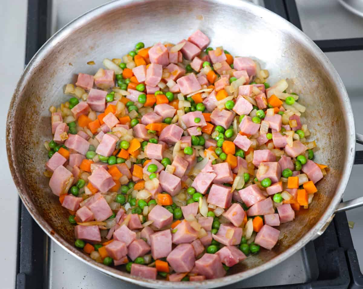 I know how much you guys love my fried rice recipes, and this Ham Fried Rice is a classic! Just toss in leftover rice, ham, and a few simple ingredients, itโs ready in under 30 minutes! Onions, ham, peas and carrots all sautรฉing in a skillet.