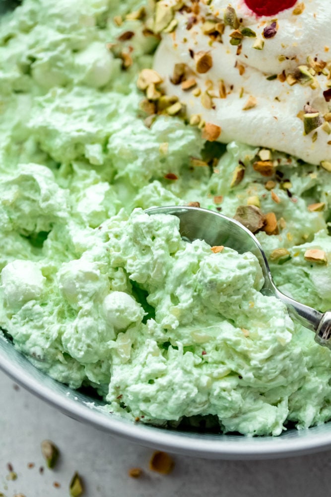 This pistachio pudding salad is a super easy and delicious dessert made with only 5 ingredients! Sweet and simple and bursting with pineapple, pistachio and marshmallow flavors, you will have a new favorite dessert salad after you try this recipe! Up close photo of pistachio pudding in a bowl with a silver spoon on the side.