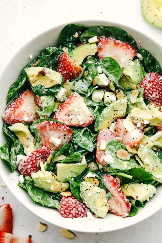 Fresh strawberries, sliced avocados, slivered almonds and sprinkled with feta cheese all tossed with a spinach salad then drizzled poppyseed dressing mixed together for the final touch. This strawberry avocado spinach salad is one everyone is raving about! Strawberry, avocado spinach salad with poppyseed dressing mixed together in a white bowl.