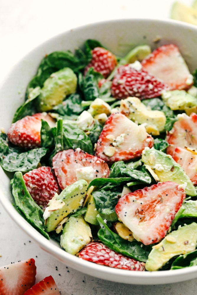 Fresh strawberries, sliced avocados, slivered almonds and sprinkled with feta cheese all tossed with a spinach salad then drizzled poppyseed dressing mixed together for the final touch. This strawberry avocado spinach salad is one everyone is raving about! Strawberry avocado spinach salad tossed together in a white bowl and ready to serve.