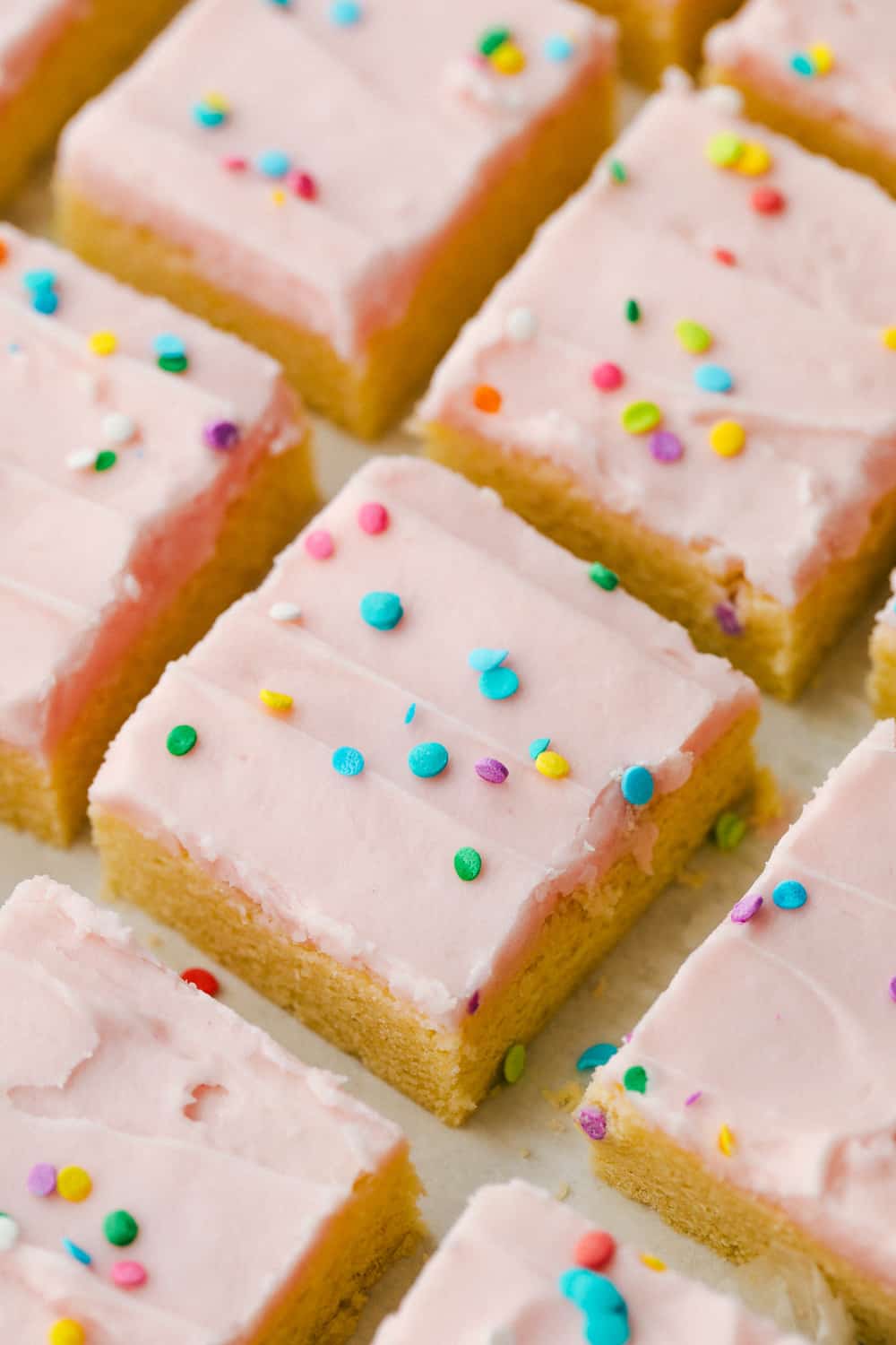 These sugar cookie bars are soft and sweet with a smooth layer of icing that is sprinkled on top. Perfect for your next party! Sugar cookie bars cut into squares with sprinkles on top.