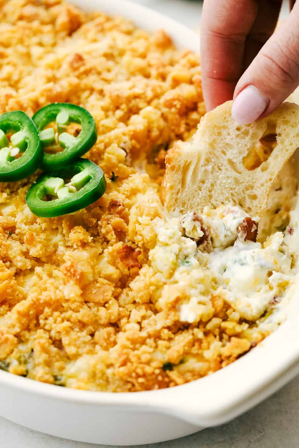 Jalapeno Popper Dip takes all the flavor of the popper and turns it into a creamy, cheesy, easy to eat dip. Super effortless and full of enticing flavors, this dip will be the star of the party!ย Dipping bread into the creamy jalapeno dip.