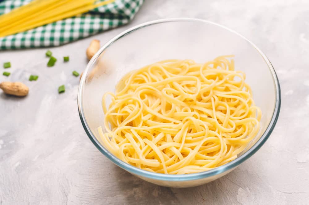 Thai Peanut Sesame Noodlesย is an asianย favorite that combines creamy peanut butter, soy sauce,ย sesame oil, minced garlic all mixed with linguine noodles tossed in this amazingly sweet and savoryย sauce.ย Cooked linguine in a glass bowl.