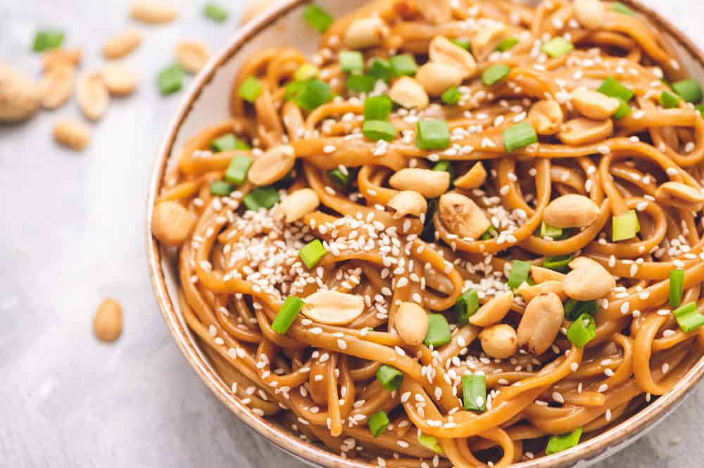 Thai Peanut Sesame Noodlesย is an asianย favorite that combines creamy peanut butter, soy sauce,ย sesame oil, minced garlic all mixed with linguine noodles tossed in this amazingly sweet and savoryย sauce.ย Thai peanut sesame noodles in a bowl with peanut halves garnished with scallops and sesame seeds.