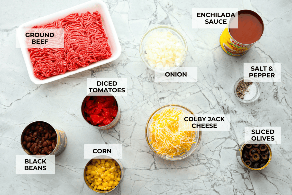 This beef enchilada dip packs all of my favorite things into one dish. It starts with red enchilada sauce, savory beef, olives, and sweet corn smothered in melty cheese. Grab your favorite tortilla chips and get dipping. Overhead shot of labeled ingredients.