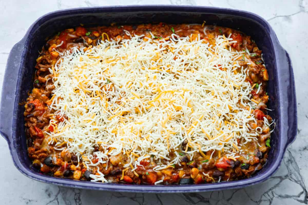This beef enchilada dip packs all of my favorite things into one dish. It starts with red enchilada sauce, savory beef, olives, and sweet corn smothered in melty cheese. Grab your favorite tortilla chips and get dipping. Overhead shot of enchilada dip with cheese sprinkled on top.