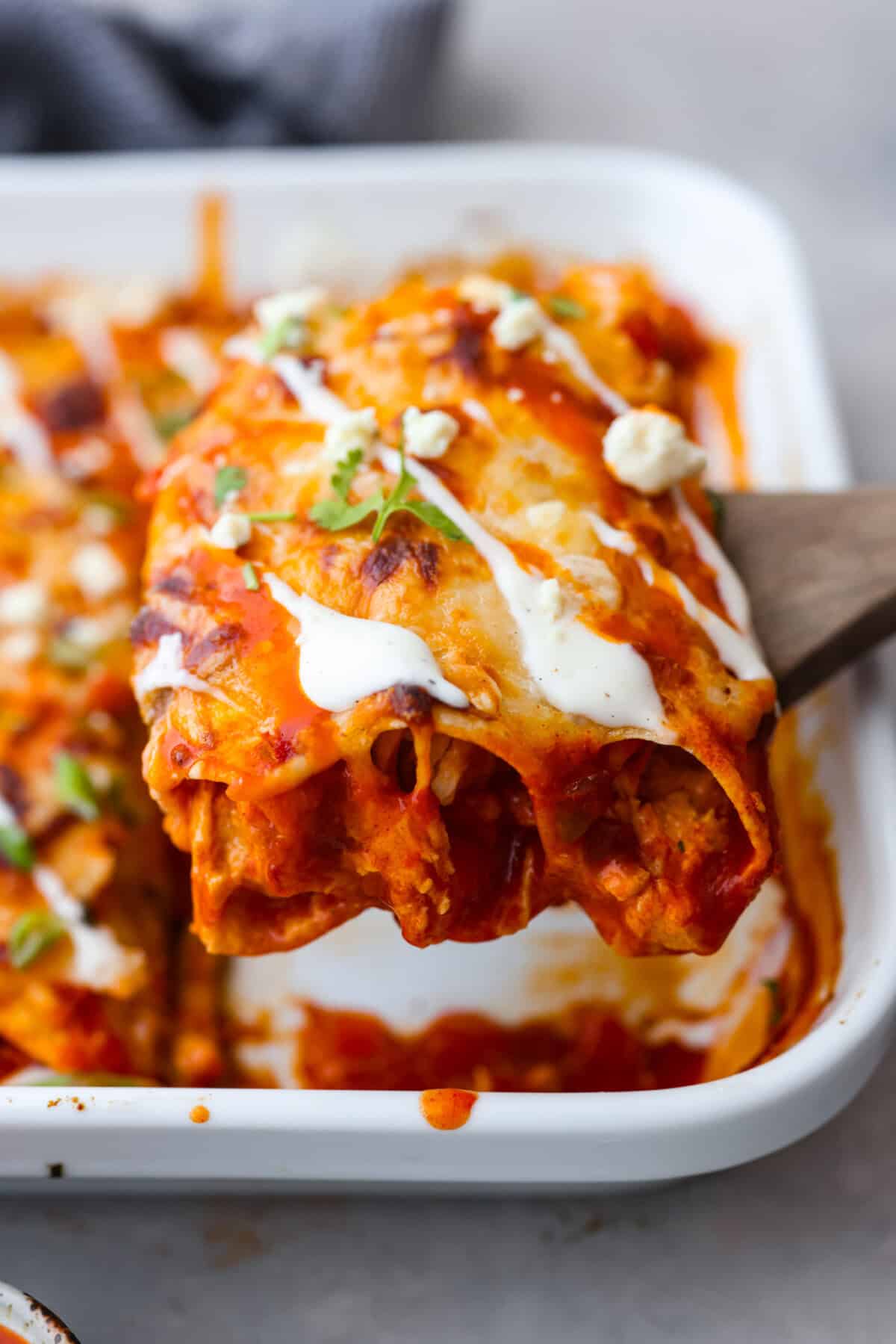A new enchilada is in town! Get ready for the bold flavors in these buffalo chicken enchiladas! Chicken enchiladas loaded with cheese and smothered in a creamy buffalo enchilada sauce. Close side view of buffalo chicken enchiladas on a serving spatula.