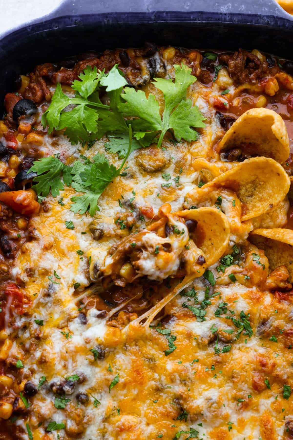This beef enchilada dip packs all of my favorite things into one dish. It starts with red enchilada sauce, savory beef, olives, and sweet corn smothered in melty cheese. Grab your favorite tortilla chips and get dipping. Close up shot of beef enchilada dip.