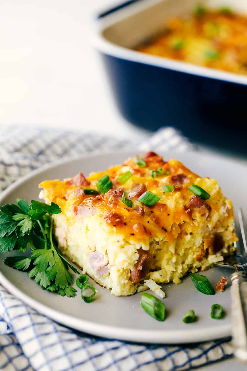 The Best Breakfast Casserole is a thick and creamy egg base with shreddedย potatoes, chunks of ham and flavorful cheese blends that bakes up in no time. Make ahead or enjoy the morning of during the holidays! Angle shot of a plated slice of casserole.