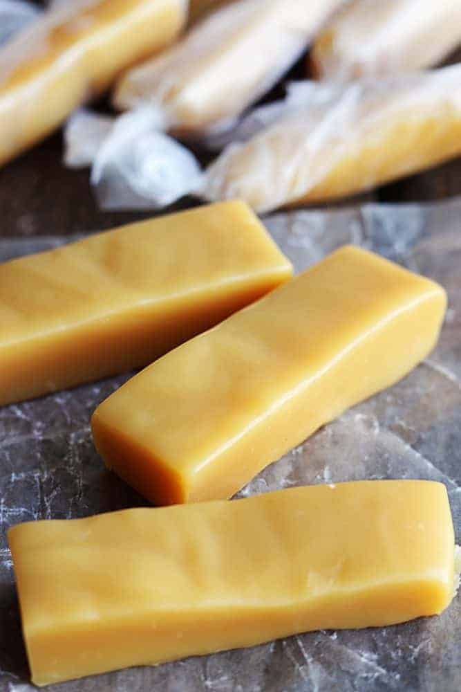 Microwave Caramels are so incredibly easy to make and they turn out perfect! Soft chewy and perfect caramel texture made right in your microwave!ย Unwrapped Microwave Caramels pieces with wrapped microwave caramels behind them.
