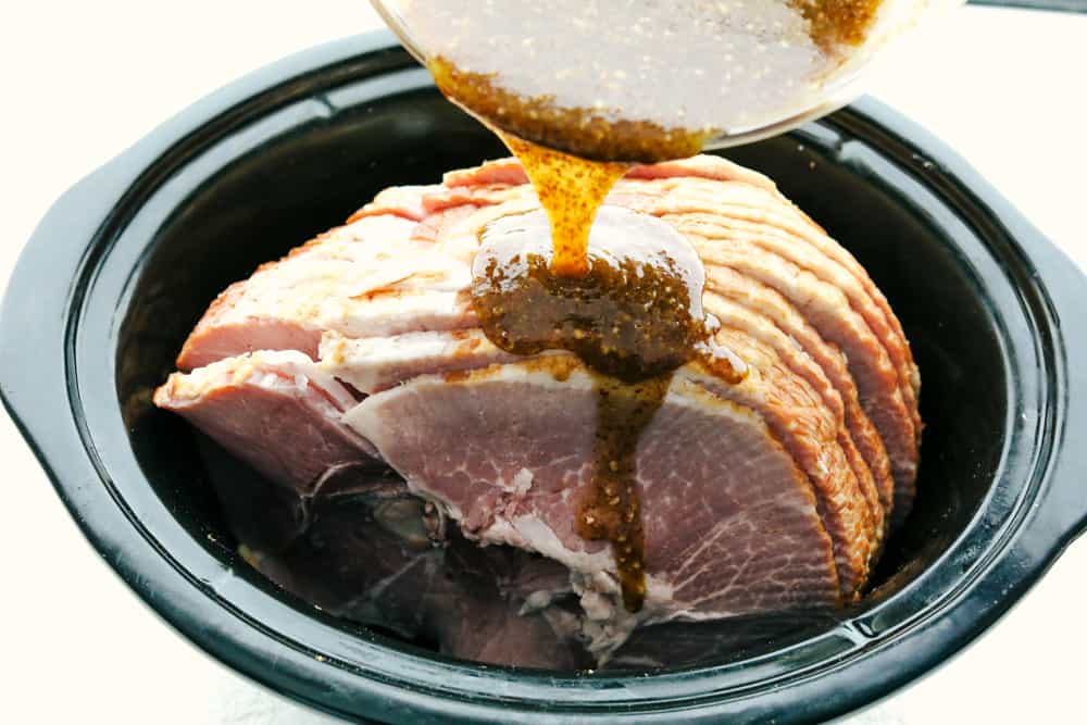 Slow Cooker Honey Garlic Mustard Glazed Ham is the perfect merge of sweet, salty and a touch of spice. This super easy, gorgeously glazed ham will be the talk of the table, with a flavor so divine, it's sure to impress. Pouring honey, mustard, and garlic glaze over the ham in a crock pot.