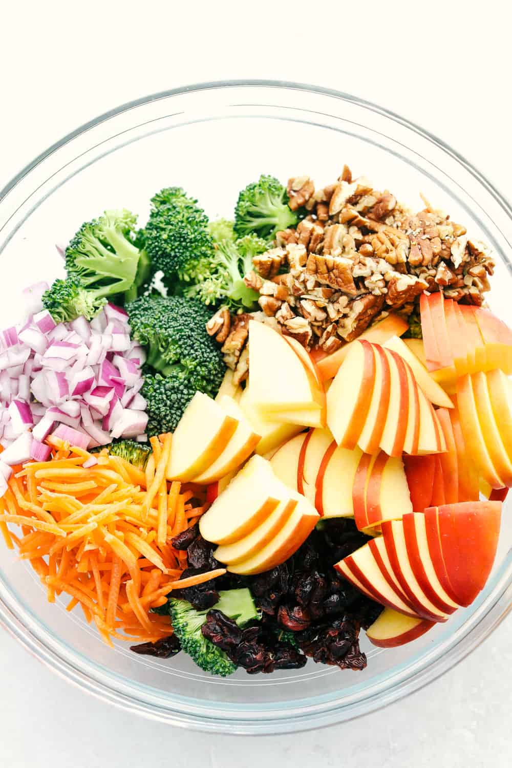 Broccoli, pecans, cranberries, carrots and apples come together to make an amazing salad with delicious flavors and textures. The creamy dressing on top makes this salad absolutely incredible! The ingredients to make broccoli apple salad in a bowl ready to combine.