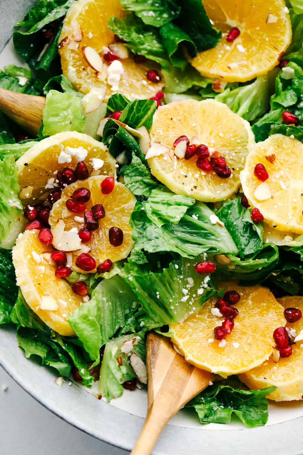Orange Pomegranate Salad is a delicious mix of greens with fresh oranges, pomegranates and topped with feta cheese and an amazing orange vinaigrette dressing. If you are looking for an awesome salad that is fresh and full of tempting and unique flavors, then this salad is for you! Mixing the ingredients for the Orange Pomegranate salad with Orange vinaigrette dressing.