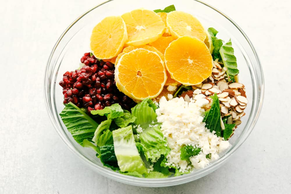 Orange Pomegranate Salad is a delicious mix of greens with fresh oranges, pomegranates and topped with feta cheese and an amazing orange vinaigrette dressing. If you are looking for an awesome salad that is fresh and full of tempting and unique flavors, then this salad is for you! The ingredients ready to toss in the Orange Pomegranate Salad.