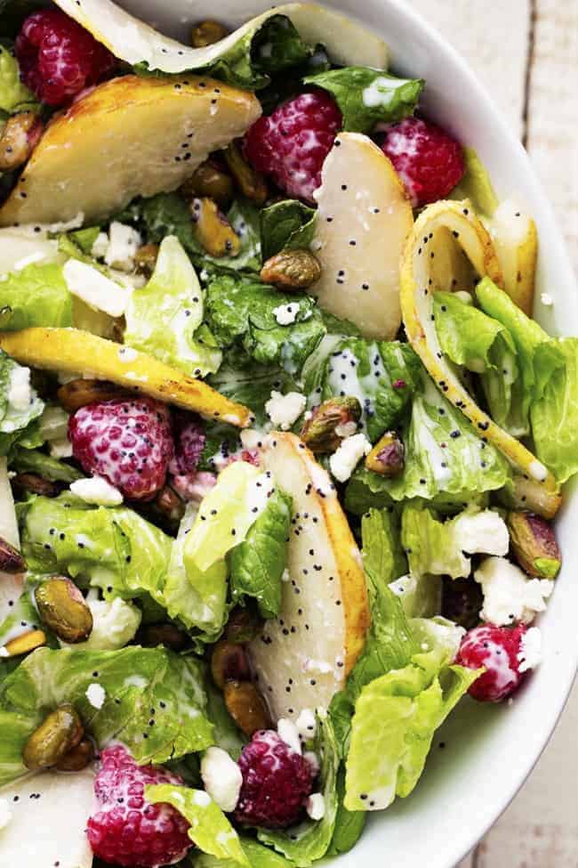 A delicious and healthy salad filled with raspberries, pears, and pistachios add a delicious flavor and crunch! pear raspberry pistachio salad in a white bowl.