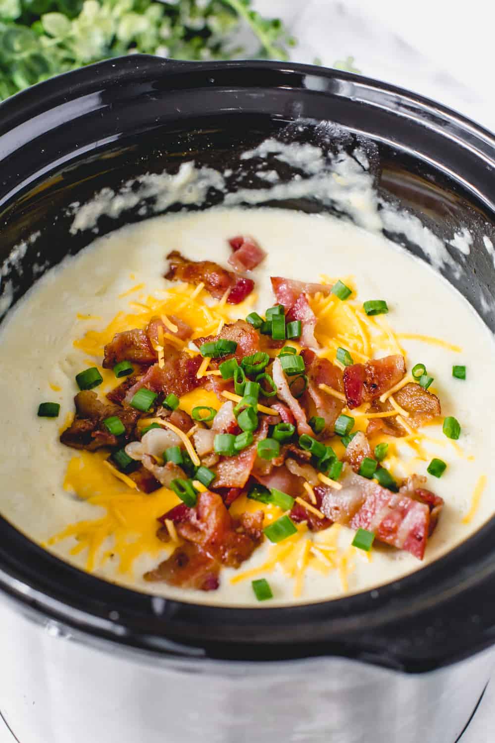 Slow Cooker Loaded Baked Potato Soup is hands down the best loaded baked potato soup that I have ever had. ย Creamy and delicious with all of the goodness of a baked potato and made right in your slow cooker! Slow cooker loaded baked potato soup in a slow cooker garnished with chopped bacon, cheese and onions.