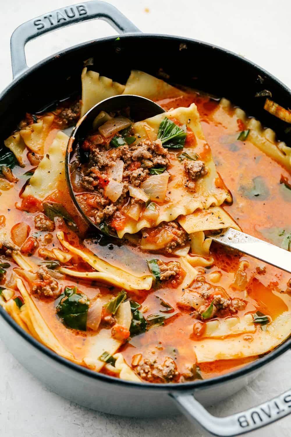 This lasagna soup recipe has all the flavors of classic lasagna packed into a warm and comforting soup! It is full of tender noodles, savory ground beef, rich marinara sauce, and melty cheese. It's a delicious meal that your family will adore and want to enjoy again and again! Close up shot of a pot of lasagna soup with a ladle dishing up a scoop.