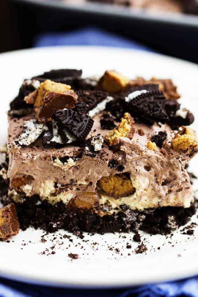 An oreo crust, a creamy peanut butter cheesecake center with peanut butter cups, and a chocolate pudding whipped topping. And noย baking required! Can you see why this is heaven? peanut butter chocolate delight on a white plate.