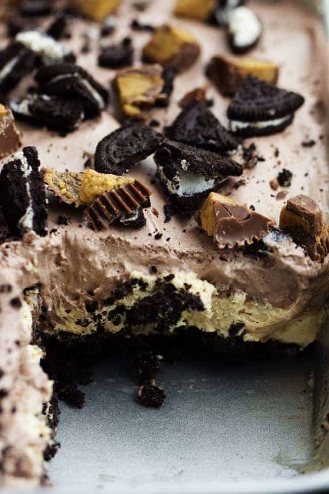 An oreo crust, a creamy peanut butter cheesecake center with peanut butter cups, and a chocolate pudding whipped topping. And noย baking required! Can you see why this is heaven? peanut butter chocolate delight on a tray with one piece missing.