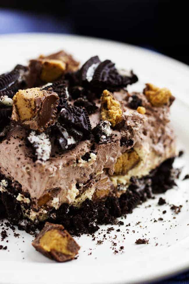 An oreo crust, a creamy peanut butter cheesecake center with peanut butter cups, and a chocolate pudding whipped topping. And noย baking required! Can you see why this is heaven? peanut butter chocolate delight on a white plate.