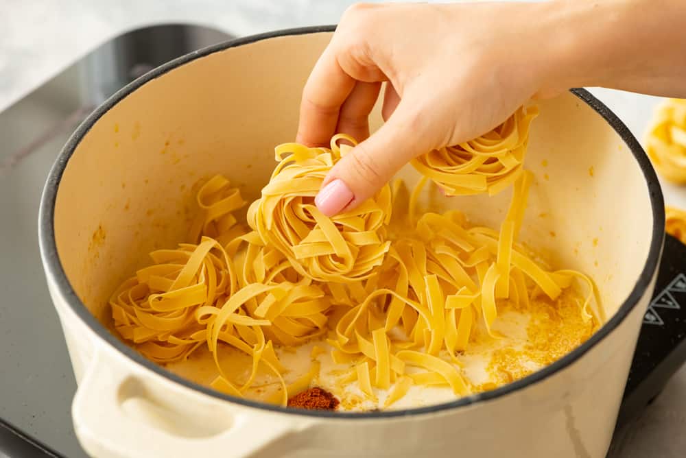 One Pot Cajun Chicken Alfredo Pasta is anย amazing one pot meal that is on the dinner table in less than 30 minutes! ย The cajun spice adds the perfect amount of flavor to the creamy alfredo sauce! dried fettuccine noodles being added to the pot to cook