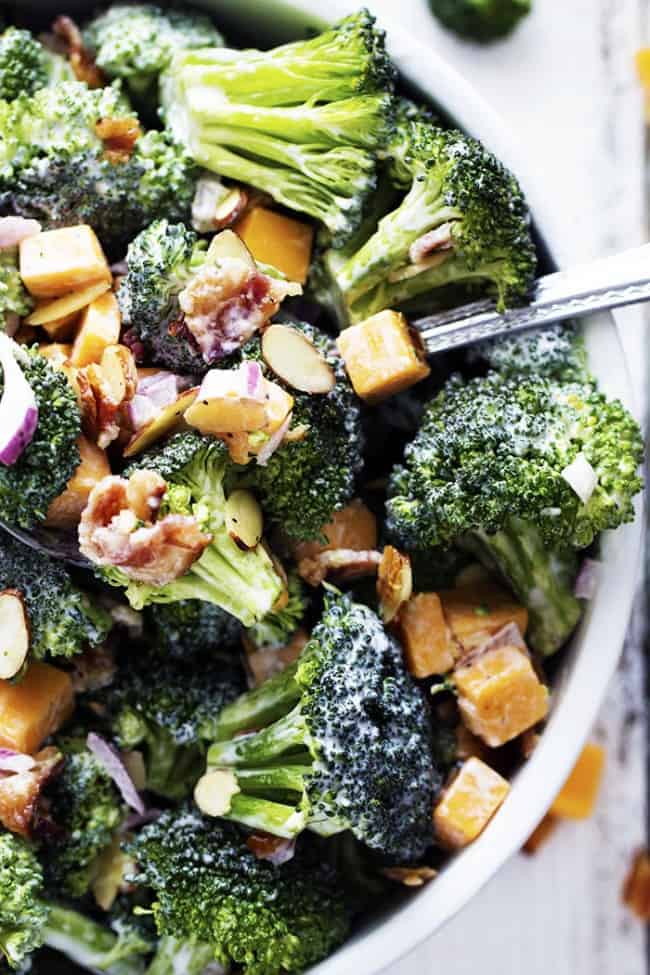 A delicious broccoli salad full of bacon, cheddar, and almonds. The creamy dressing on top is sweet and tangy and AMAZING! Creamy broccoli salad in a white bowl.
