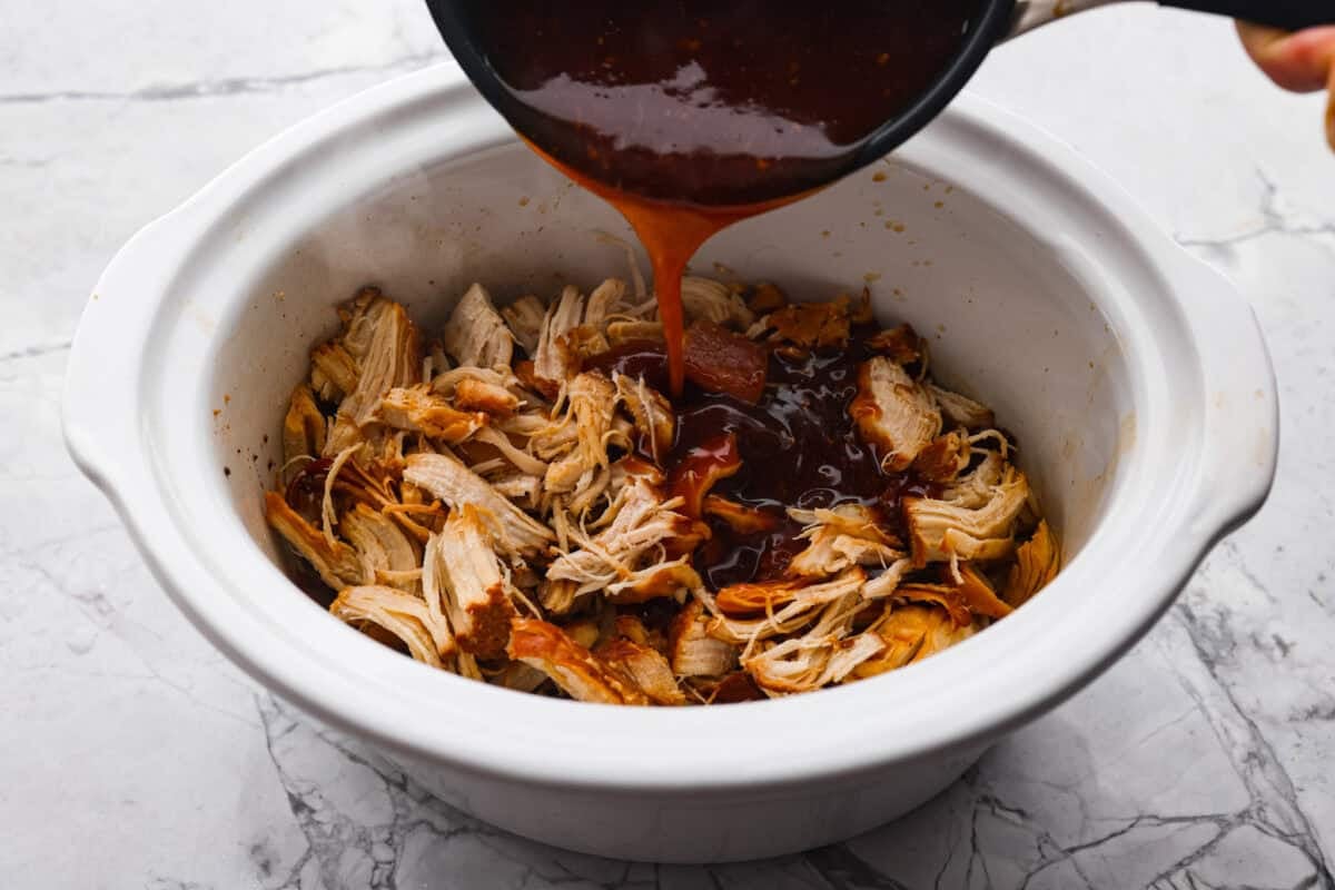 This slow cooker honey teriyaki chicken is so easy to throw together, and the flavor is out of this world! The chicken cooks to perfection and will be one of the best things you'll ever make! Angle shot of someone pouring honey teriyaki sauce over the shredded chicken in the crockpot.