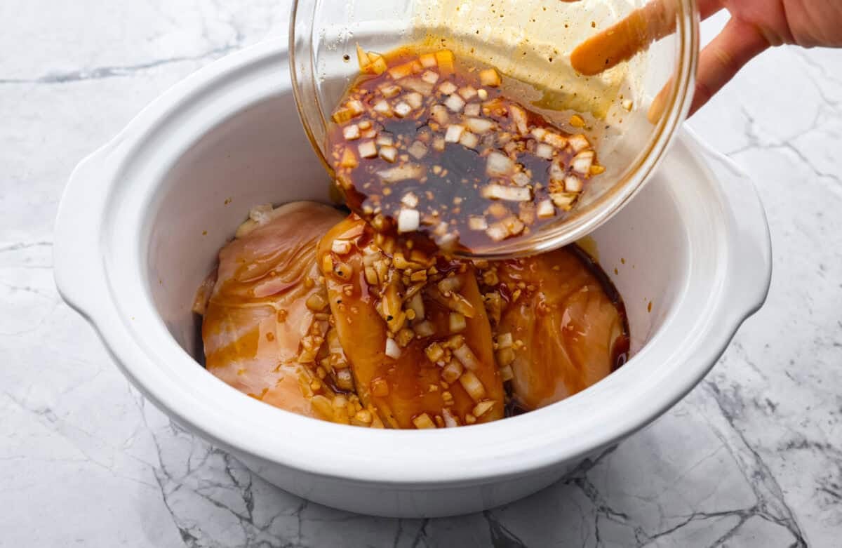 This slow cooker honey teriyaki chicken is so easy to throw together, and the flavor is out of this world! The chicken cooks to perfection and will be one of the best things you'll ever make! Angle shot of someone pouring sauce over the chicken in the crockpot.