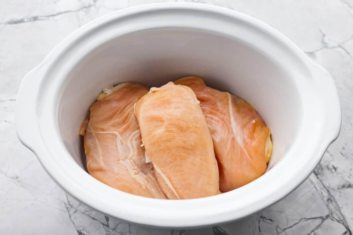 This slow cooker honey teriyaki chicken is so easy to throw together, and the flavor is out of this world! The chicken cooks to perfection and will be one of the best things you'll ever make! Overhead shot of chicken breasts in the bottom of the crock pot.