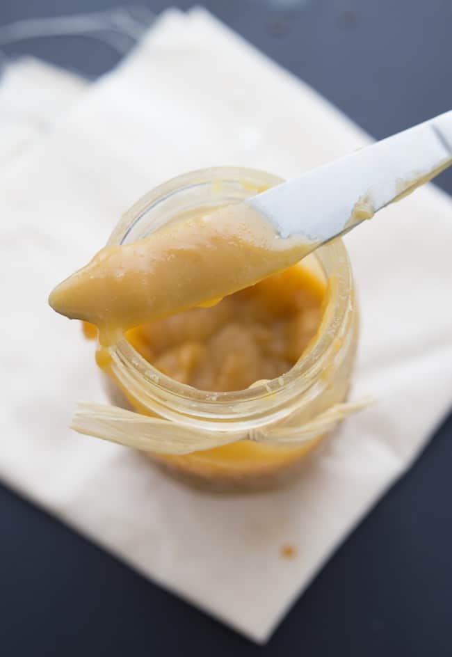 This mixture will be a thick and delicious caramel sauce! Caramel in a glass mason jar with a close up on the caramel on a stirring knife.